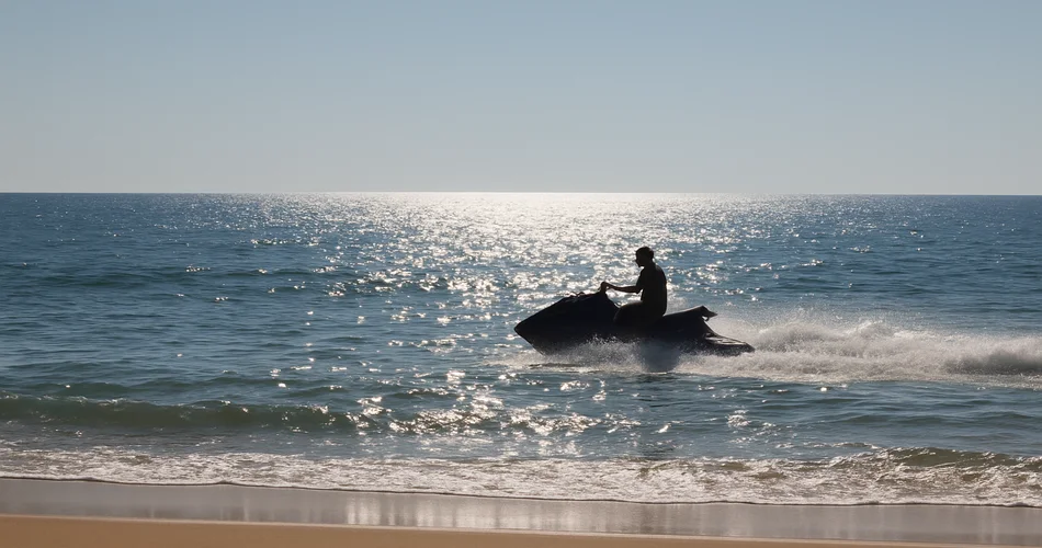 Generated image: a jet ski speeds across the water near a sandy beach.